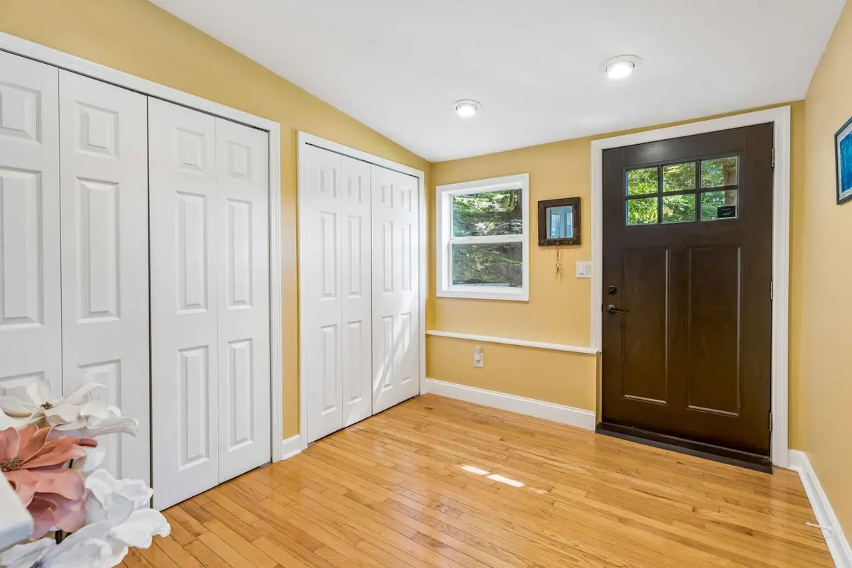 Interior entry at 26 Oak Street with a craftsman front door, two white six-panel storage closets, golden-yellow walls, and oak hardwood floors