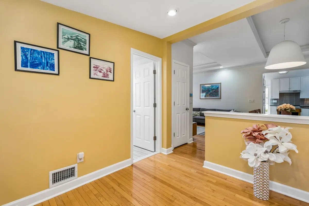 Bright entry foyer at 26 Oak Street with warm golden-yellow walls, a framed art gallery wall, oak hardwood floors, and an open sightline through to the living room and kitchen