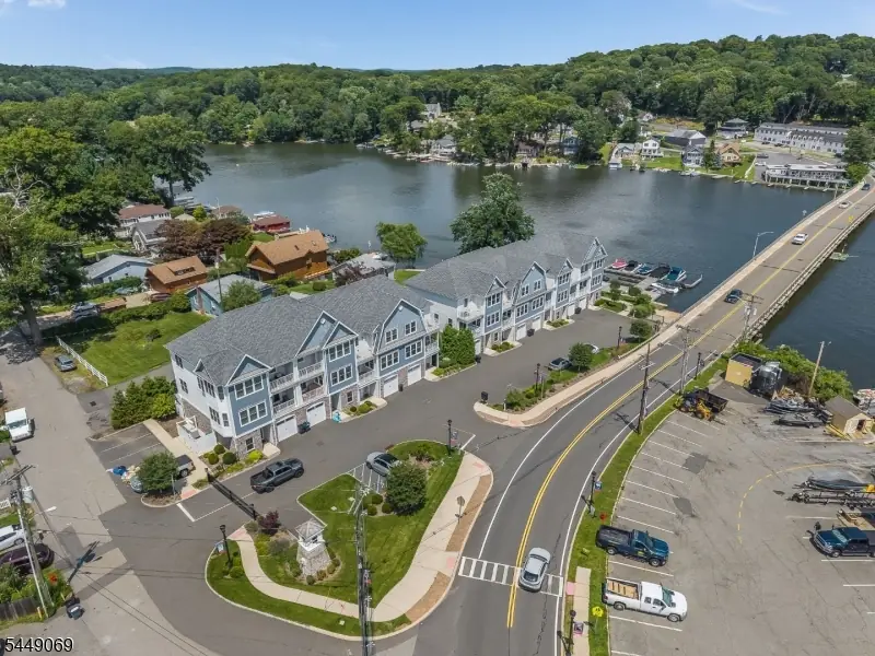 Aerial view of the Townhomes at Lakepointe on Lake Hopatcong, blue and gray three-story townhomes set on the water beside the River Styx bridge with private boat docks along the shore. Listing courtesy of Robin Dora, Prominent Properties Sotheby's International Realty.