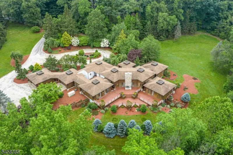 Aerial view showing the estate's dramatic star-shaped cedar rooflines around a central stone-chimney courtyard, surrounded by lawns and woodland in Blairstown