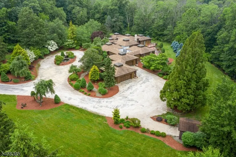 Aerial view of 51 Hoagland Road from the drive side, showing the circular crushed-stone drive, attached four-car garage, and landscaped grounds against the tree line