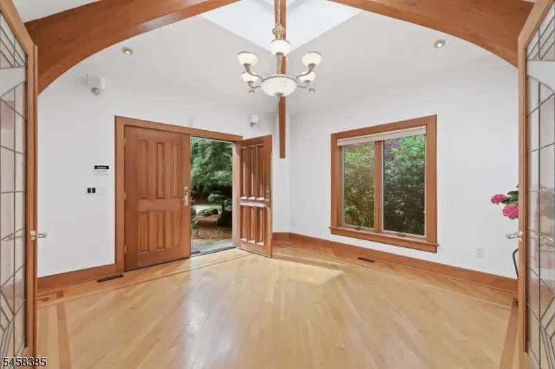 Entry foyer with a vaulted ceiling, arched wood beam, skylight, chandelier, leaded-glass sidelights, and light oak floors at 51 Hoagland Road